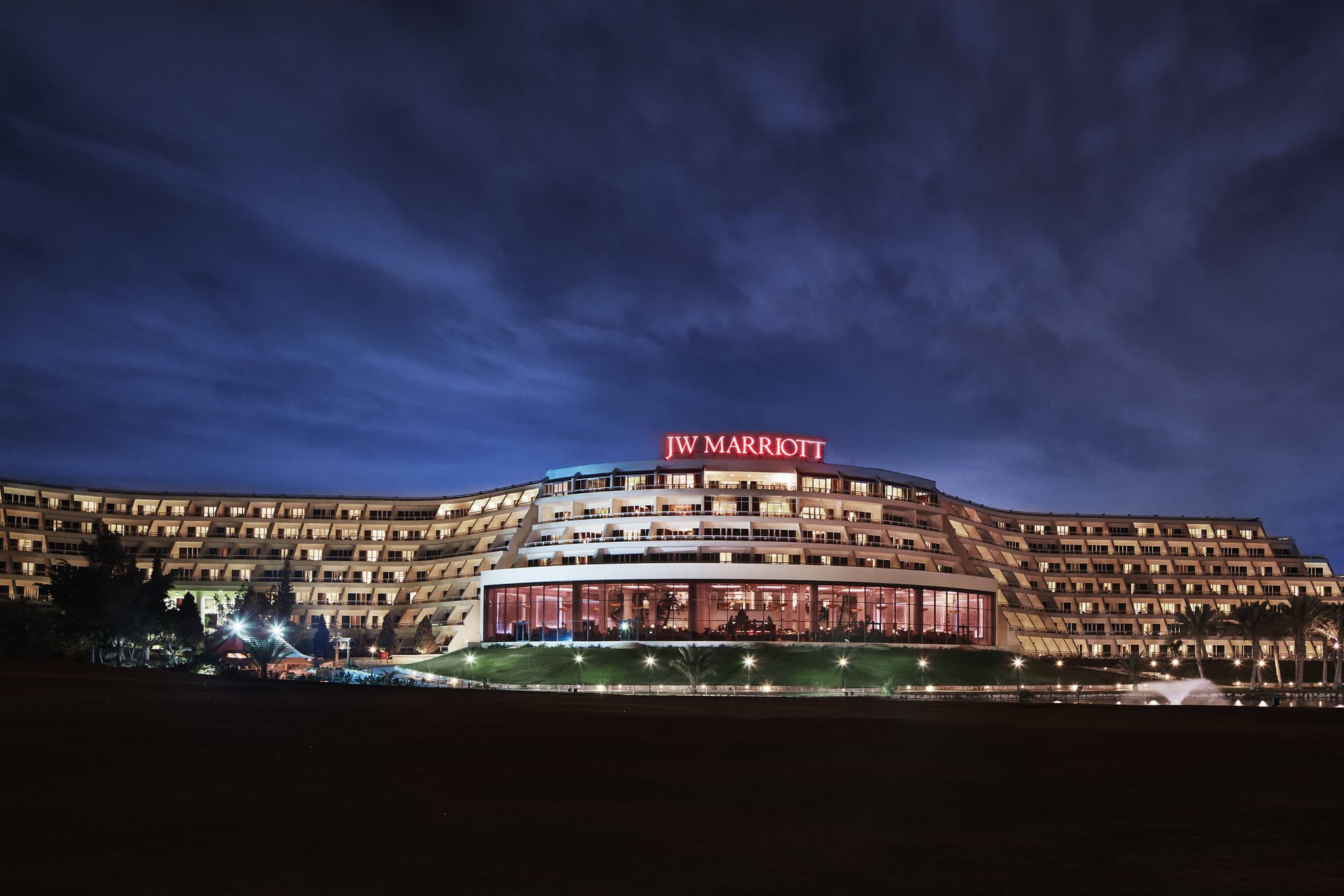 The JW Marriott Cairo's artificial beach and wave pool surrounded by palm trees and terracotta resort architecture.