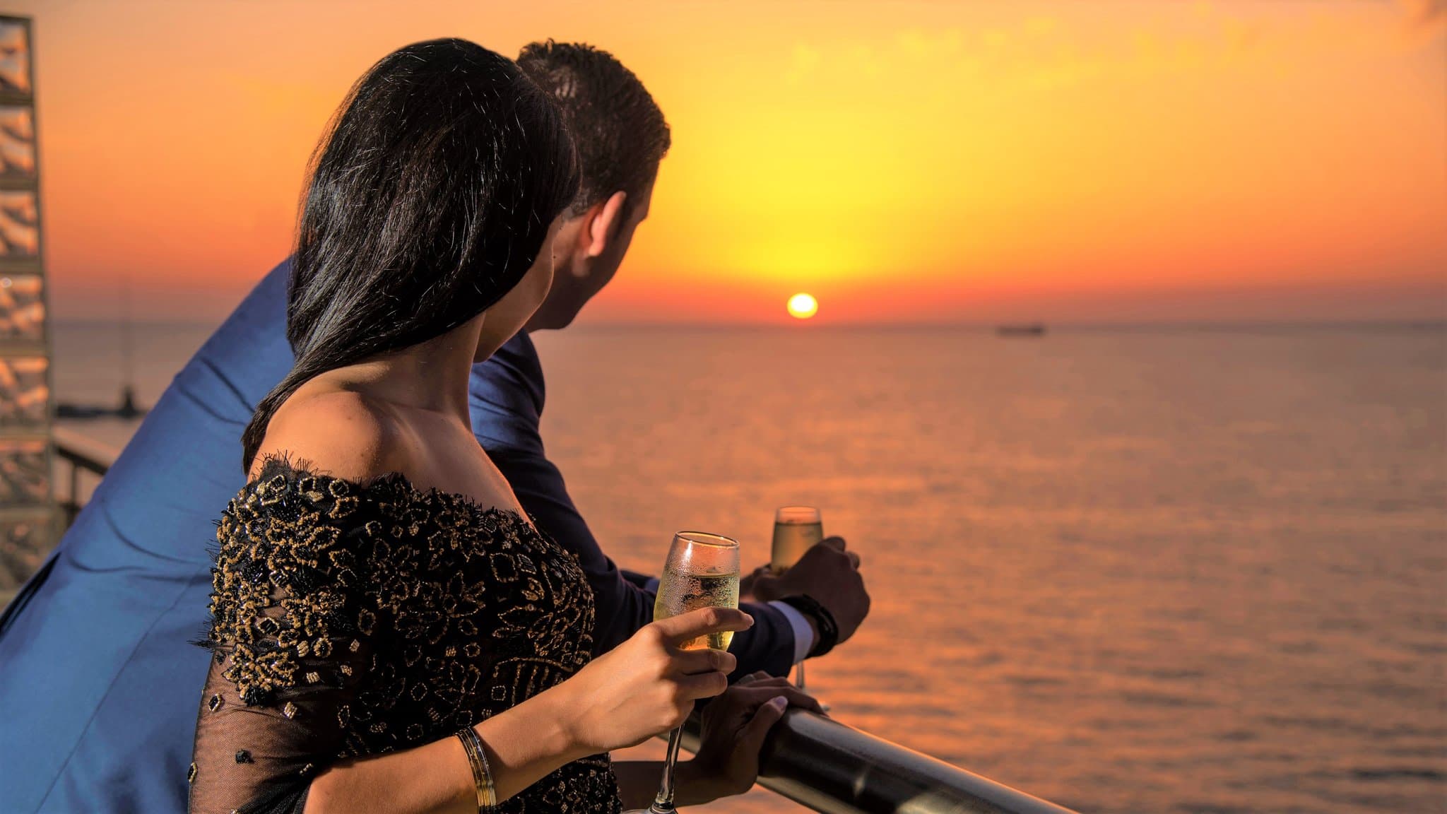 A dramatic sunset view through the curved floor-to-ceiling windows of Sydney's Club, featuring a silhouette of a dining table and the Mediterranean Sea.