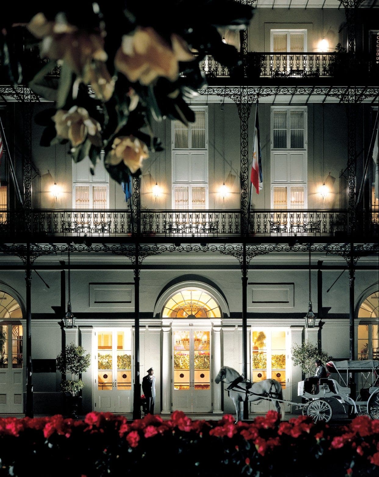 A dramatic view of the Omni Royal Orleans wrought-iron balconies overlooking a sun-drenched Royal Street, with the St. Louis Cathedral spire in the background.