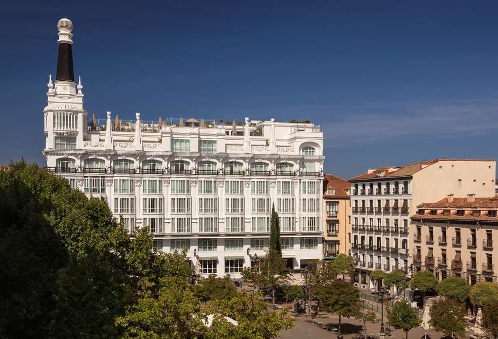 The illuminated white turret of ME Madrid Reina Victoria rising above Plaza de Santa Ana at twilight.