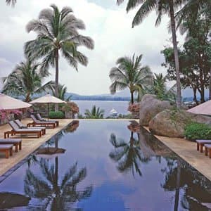 Amanpuri's iconic midnight-blue tiled swimming pool surrounded by palm trees at dusk, with Thai-style pavilions in the background.