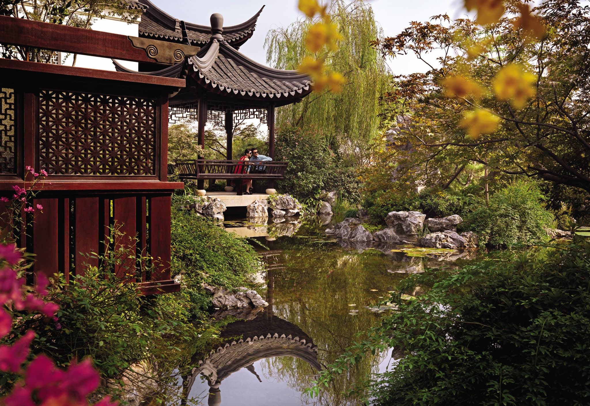 Traditional Chinese wooden pavilions with curved eaves illuminated by warm lanterns, reflecting in a calm infinity pond at twilight.