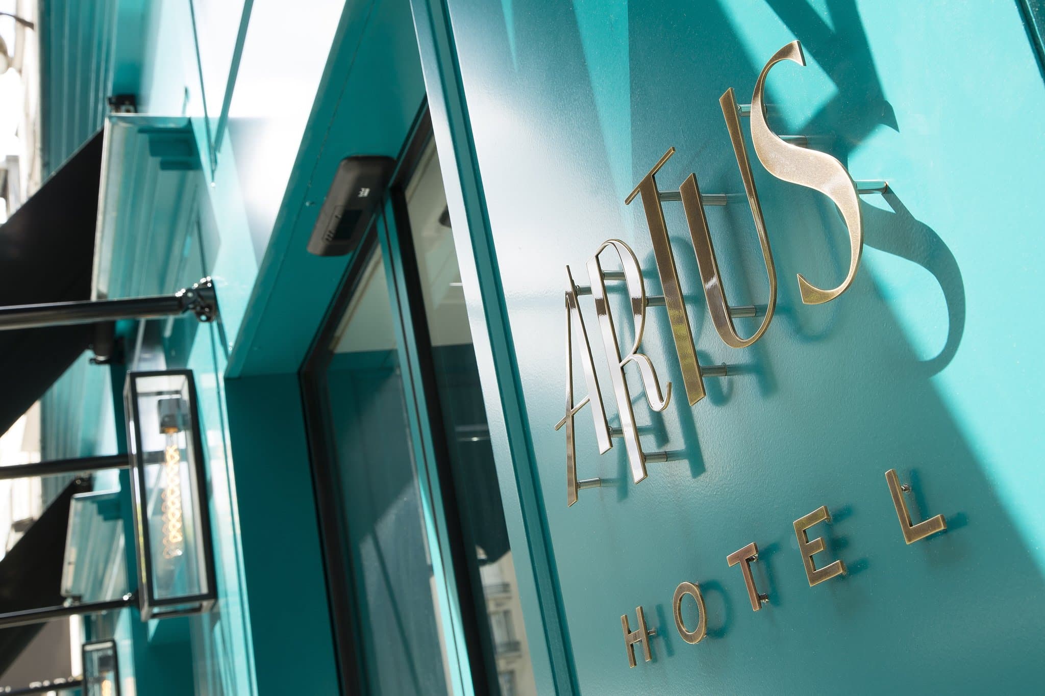 Lobby of Artus Hotel Paris featuring 1950s retro-chic design, turquoise walls, gold front desk, and a spiral staircase.