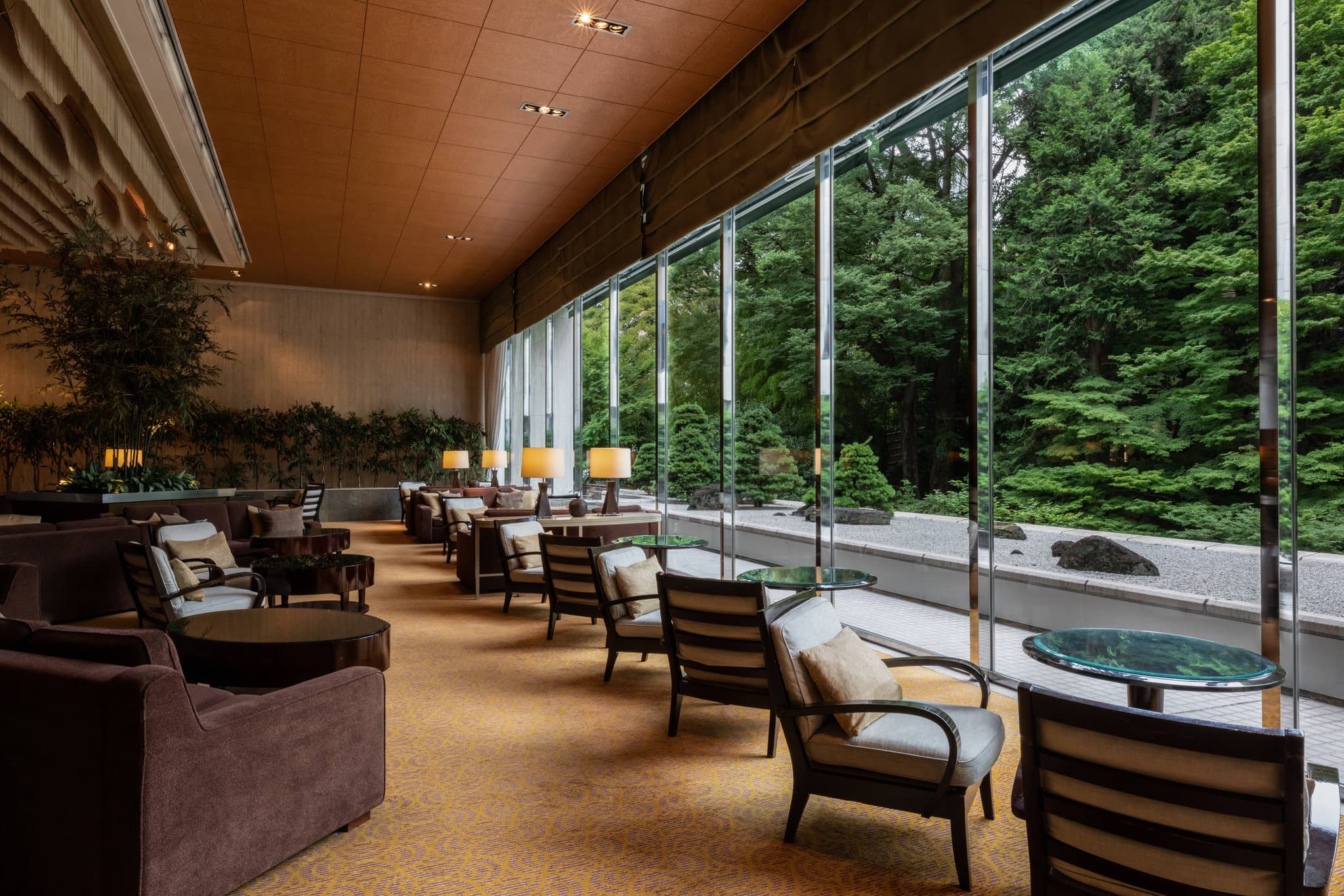 Lobby Lounge BAMBOO at Sheraton Miyako Hotel Tokyo featuring large windows looking out onto a lush, historic Japanese garden with autumn foliage.