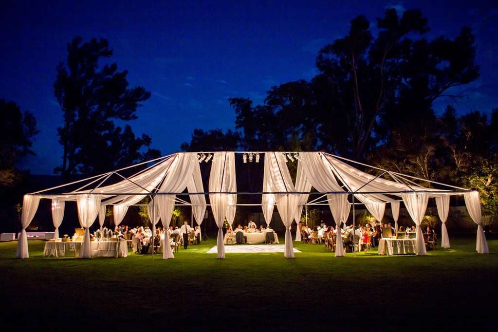 トパトパ山脈のピンク色の夕焼けを背景にしたOjai Valley Innの白いスパニッシュコロニアル様式のアーチ。前景にはランタンが灯るオークの木。