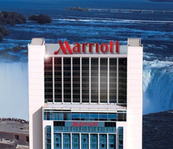 A guest bed positioned directly against a floor-to-ceiling window overlooking the mist of Niagara's Horseshoe Falls.