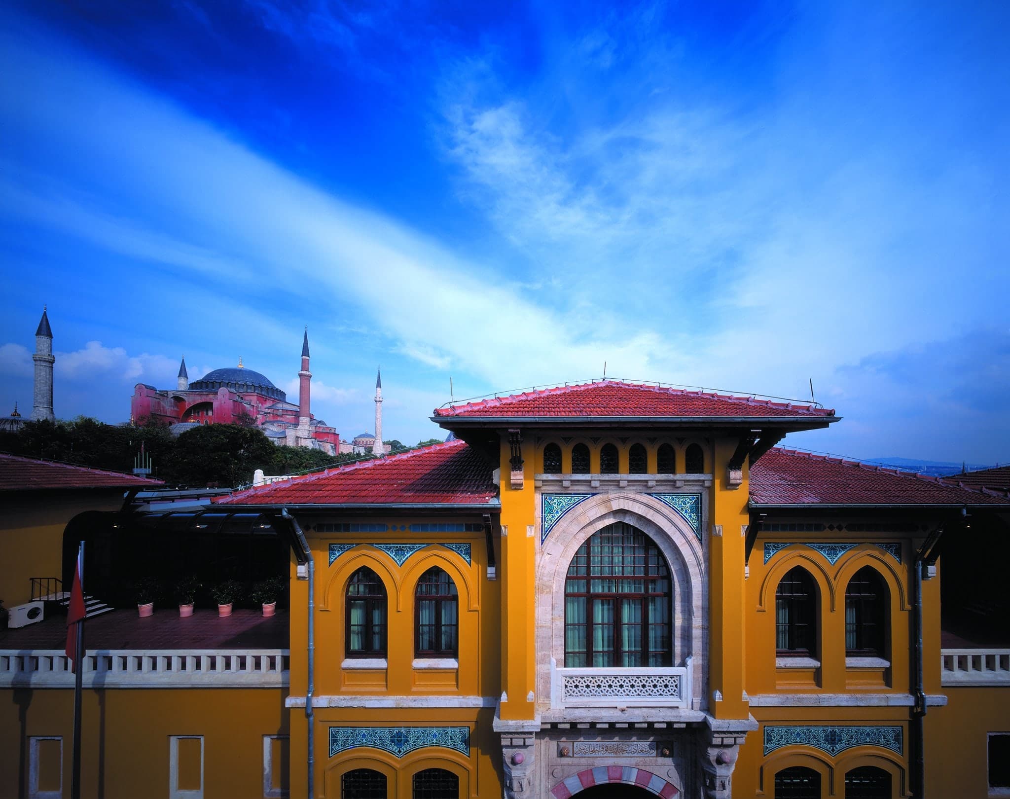 The neoclassical yellow facade of the Four Seasons Sultanahmet seen from the lush courtyard garden, framed by manicured greenery.