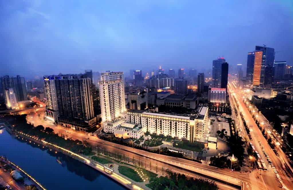 The imposing, historic facade of the Sichuan Jinjiang Hotel at dusk, featuring Soviet-influenced architecture and manicured private gardens.