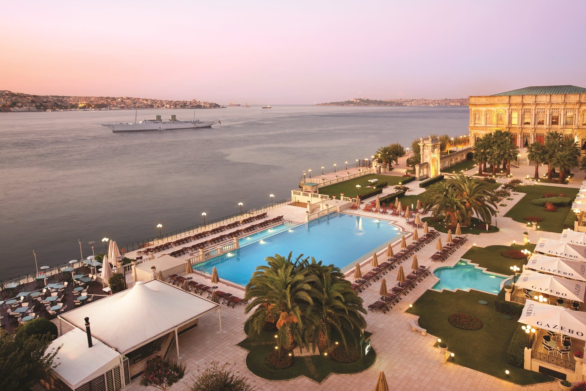 The heated infinity pool at Çırağan Palace Kempinski merging visually with the dark blue waters of the Bosphorus strait, with the illuminated Bosphorus Bridge in the background.