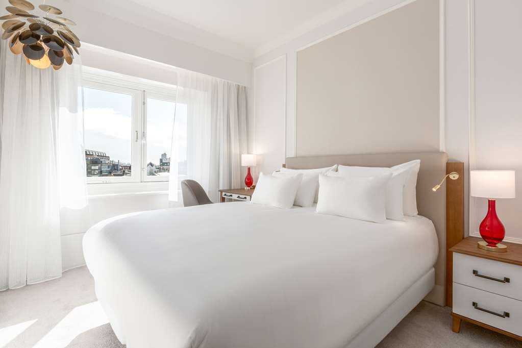 A moody, high-ceilinged hotel suite at Tivoli Doelen with a replica of Rembrandt's Night Watch on the wall and large windows overlooking the Amstel River.