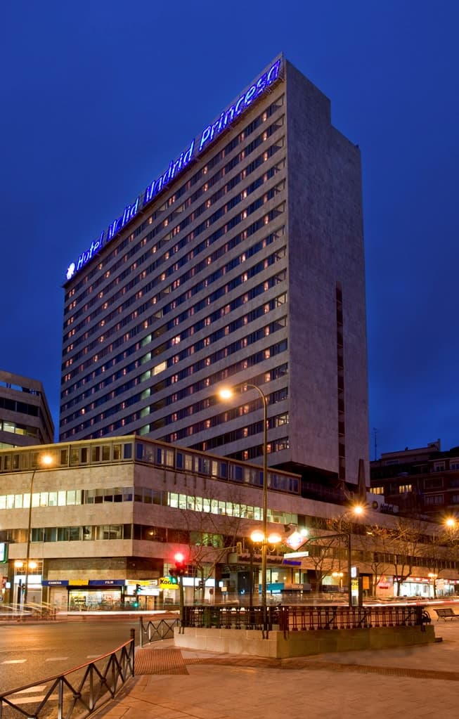 A guest soaking in a freestanding bathtub in a Meliá Madrid Princesa Level room, overlooking the Madrid skyline and Royal Palace at sunset.