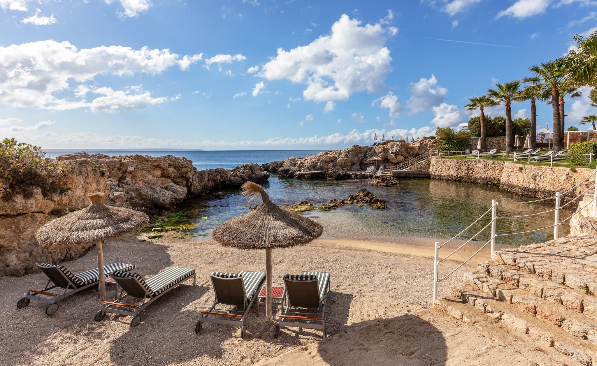 The modernist chocolate-colored facade of Hotel de Mar Gran Meliá featuring angled balconies overlooking a pine-framed turquoise cove in Mallorca.