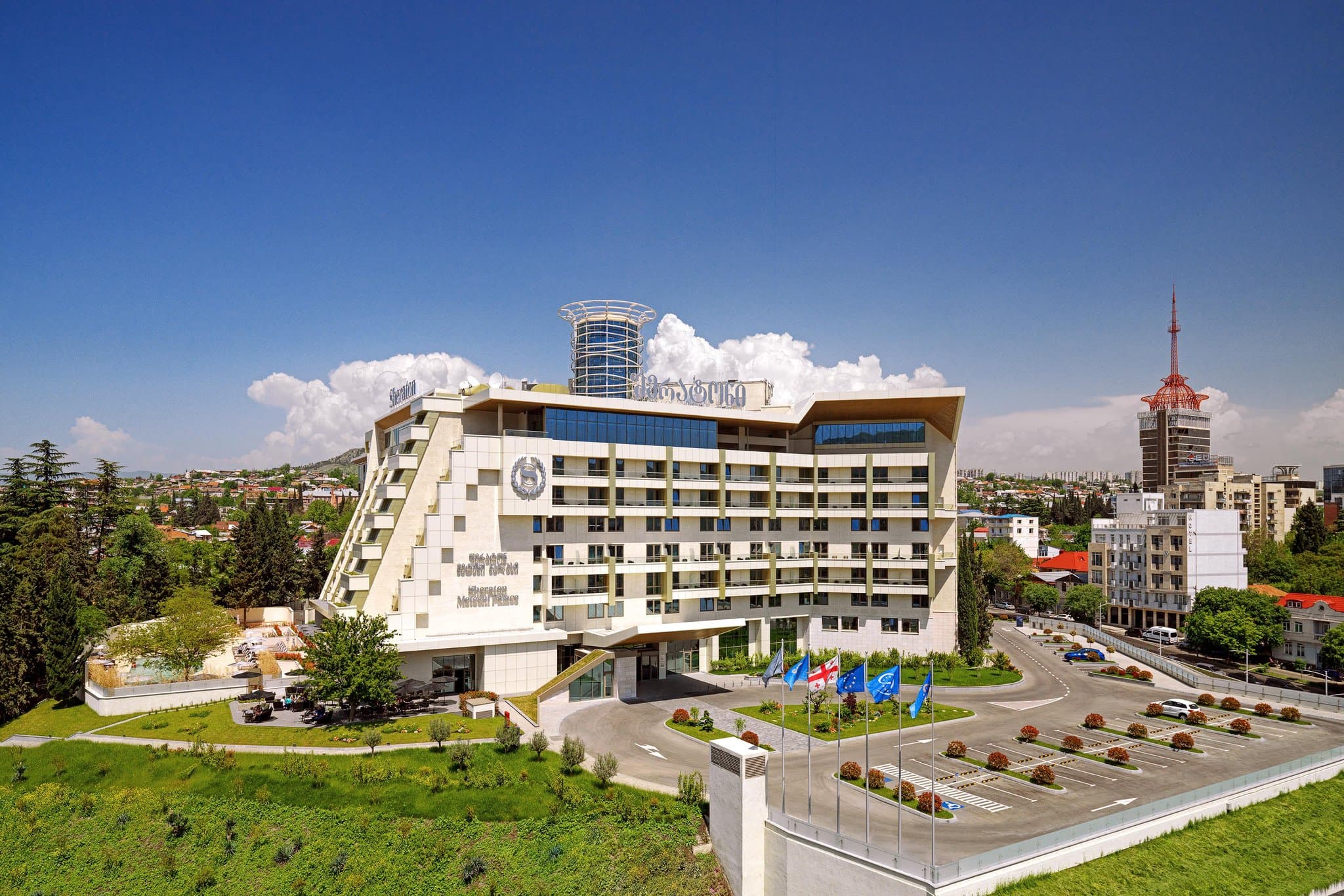 The soaring 10-story atrium lobby of Sheraton Grand Tbilisi featuring glass elevators and modern lounge seating.
