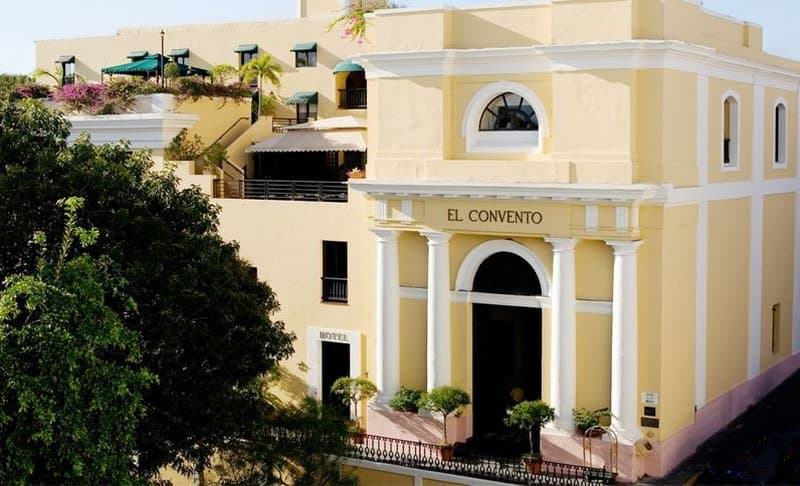 Looking down into the open-air courtyard of Hotel El Convento, featuring the massive 300-year-old Nispero tree shading diners at white-clothed tables, surrounded by Spanish colonial arches.