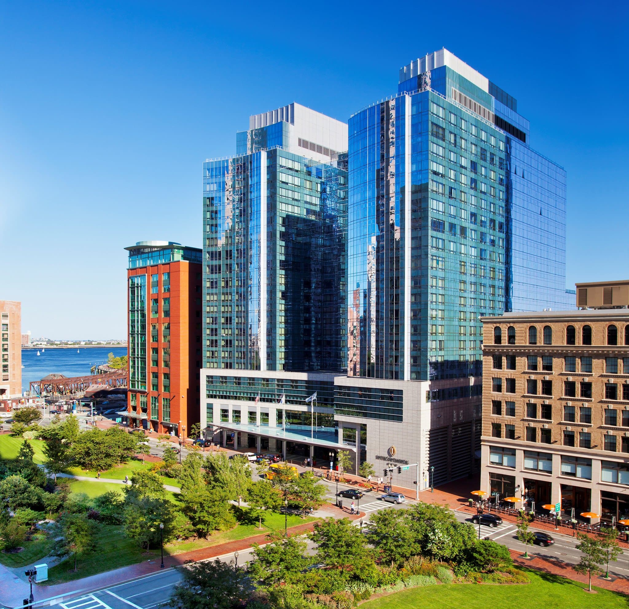 Curved glass facade of InterContinental Boston reflecting the Fort Point Channel at twilight.