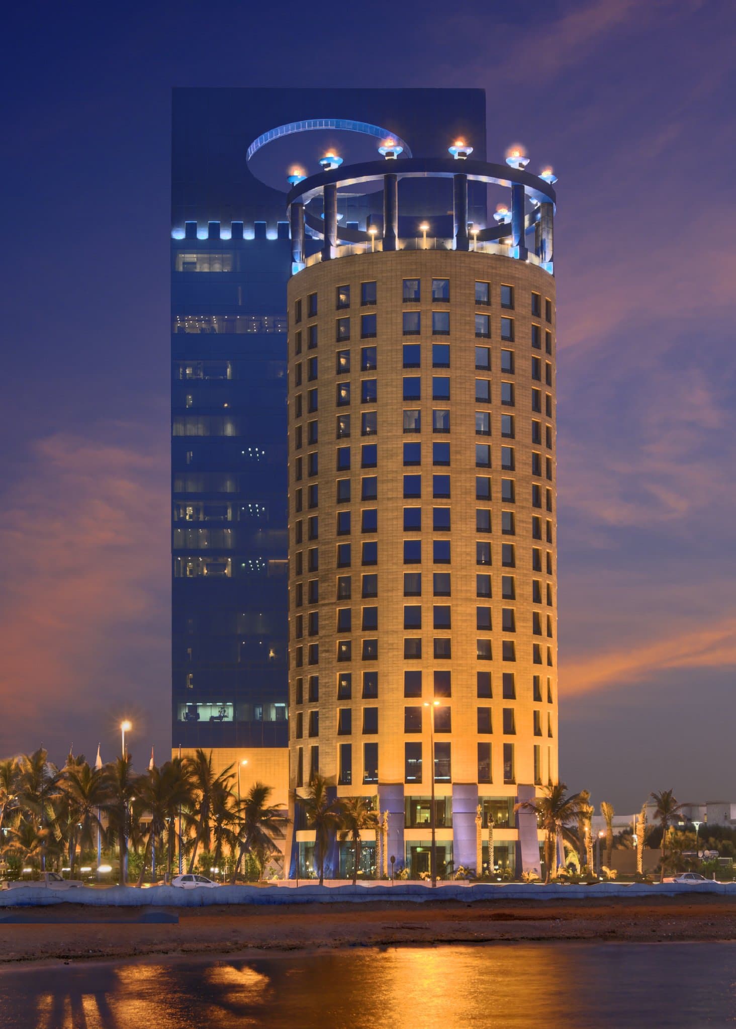 Exterior of Rosewood Jeddah at dusk featuring its signature curve, illuminated against the Red Sea coastline.