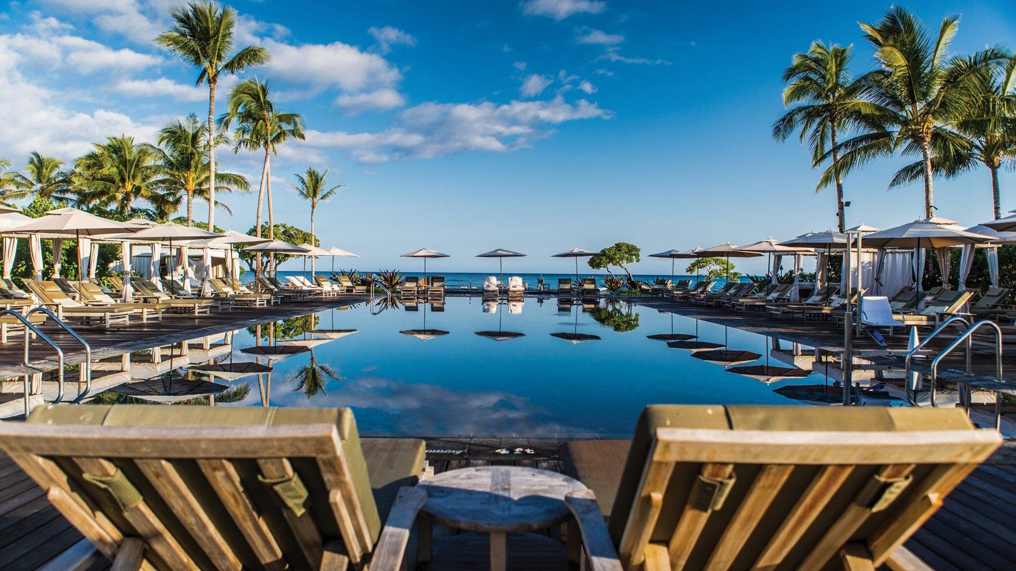 A split-level view of King's Pond at Four Seasons Hualalai showing swimmers snorkeling with tropical fish above and below the water line, surrounded by black lava rock.