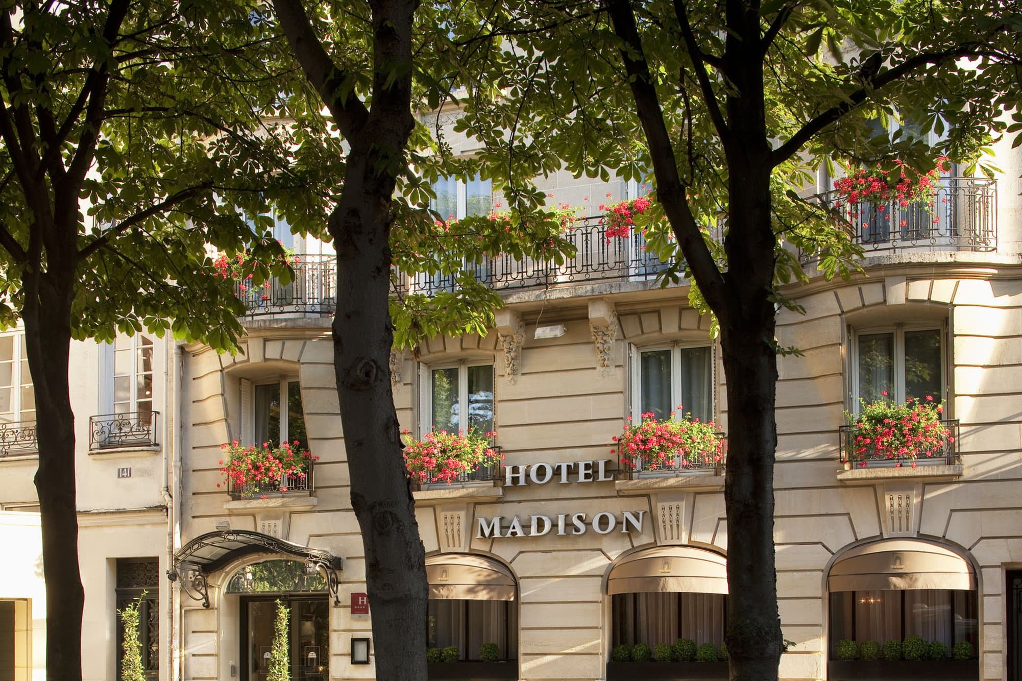 A classic wrought-iron balcony at Hotel Madison Paris framing a view of the Saint-Germain-des-Prés church tower in the morning light.