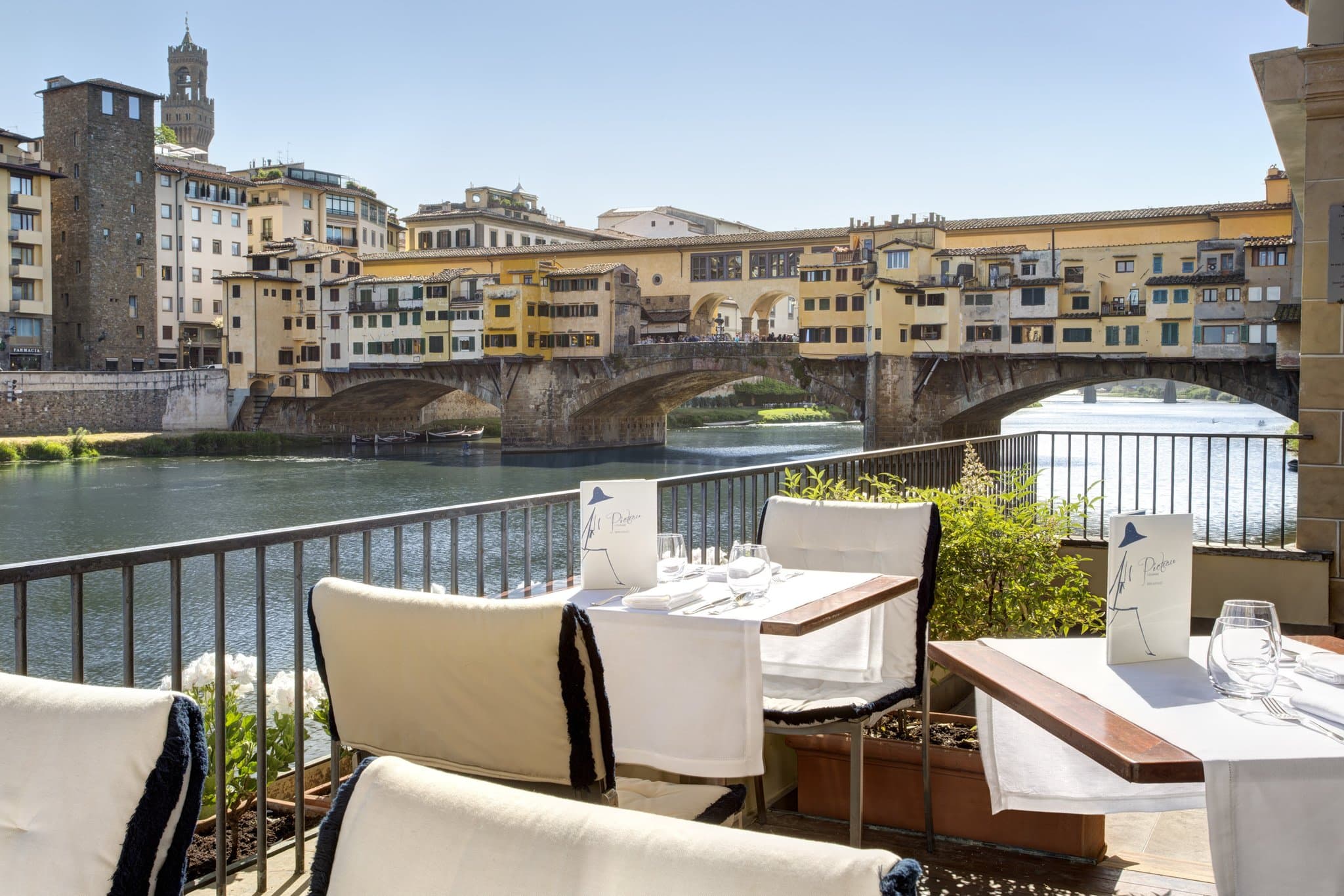 View of Hotel Lungarno's facade reflecting in the Arno River with Ponte Vecchio in the background during golden hour.