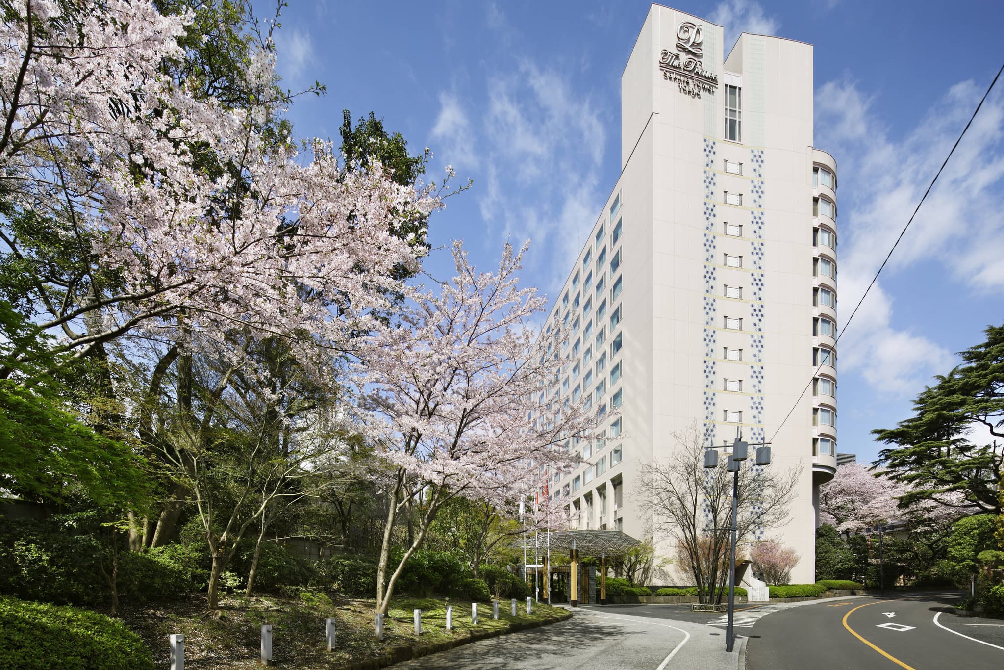 A serene view of The Prince Sakura Tower Tokyo's historic garden featuring a traditional bell tower and blooming cherry blossom trees.