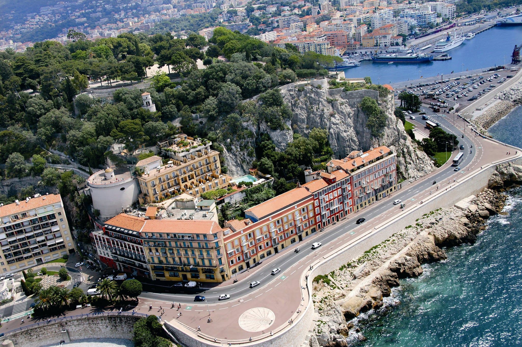 Hotel La Pérouse outdoor pool carved directly into the limestone cliff with yellow facade and green shutters.