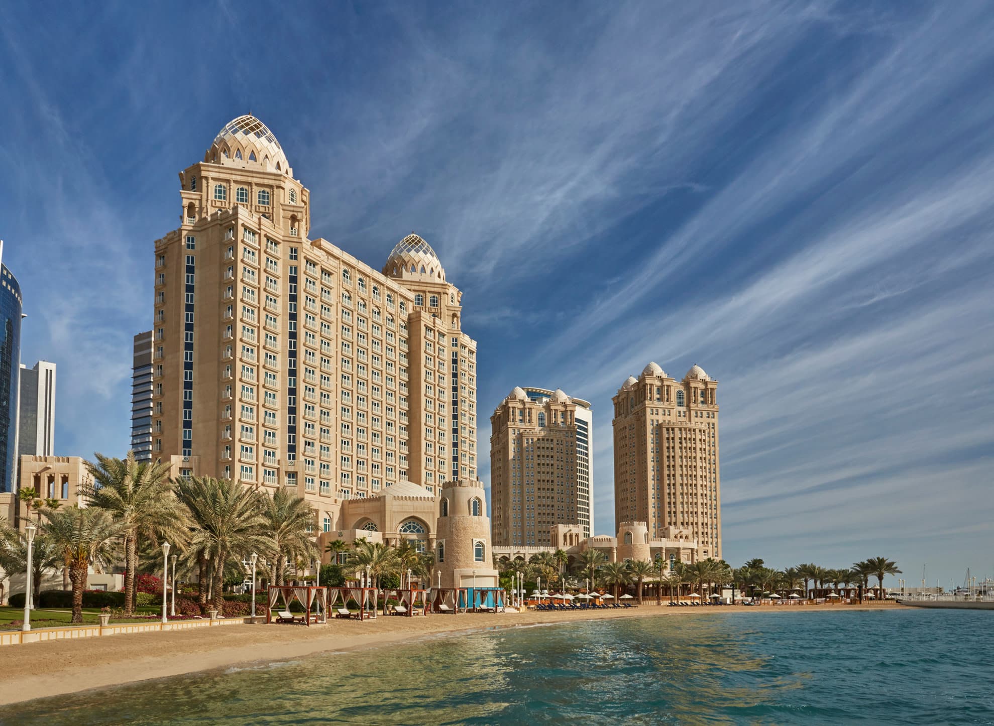 The grand three-story wellness center exterior at Four Seasons Doha, framed by palm trees and the Arabian Gulf.
