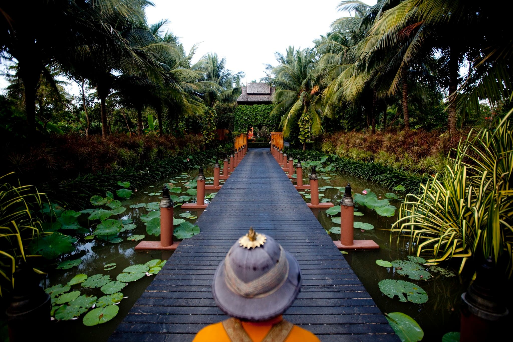 Wooden walkway crossing the Bill Bensley-designed lily pond at Anantara Bophut Koh Samui Resort at dusk.
