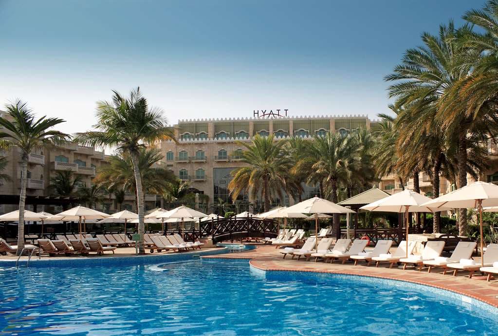 The Grand Hyatt Muscat atrium featuring a 14-meter stained-glass window casting colorful light over a bronze falconer statue and Bedouin-style tent.