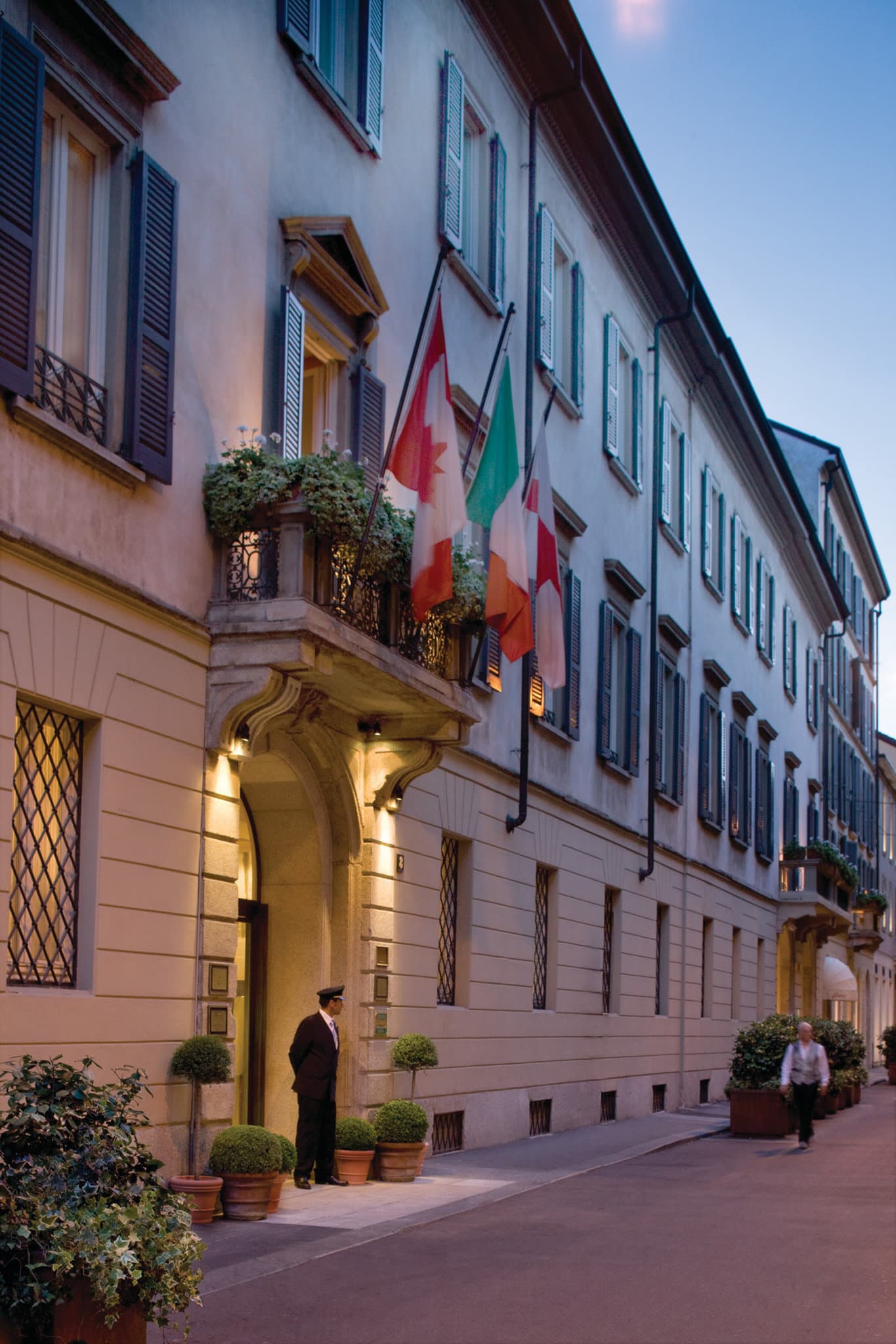 The 15th-century cloistered courtyard of Four Seasons Milan, featuring manicured hedges and stone columns.