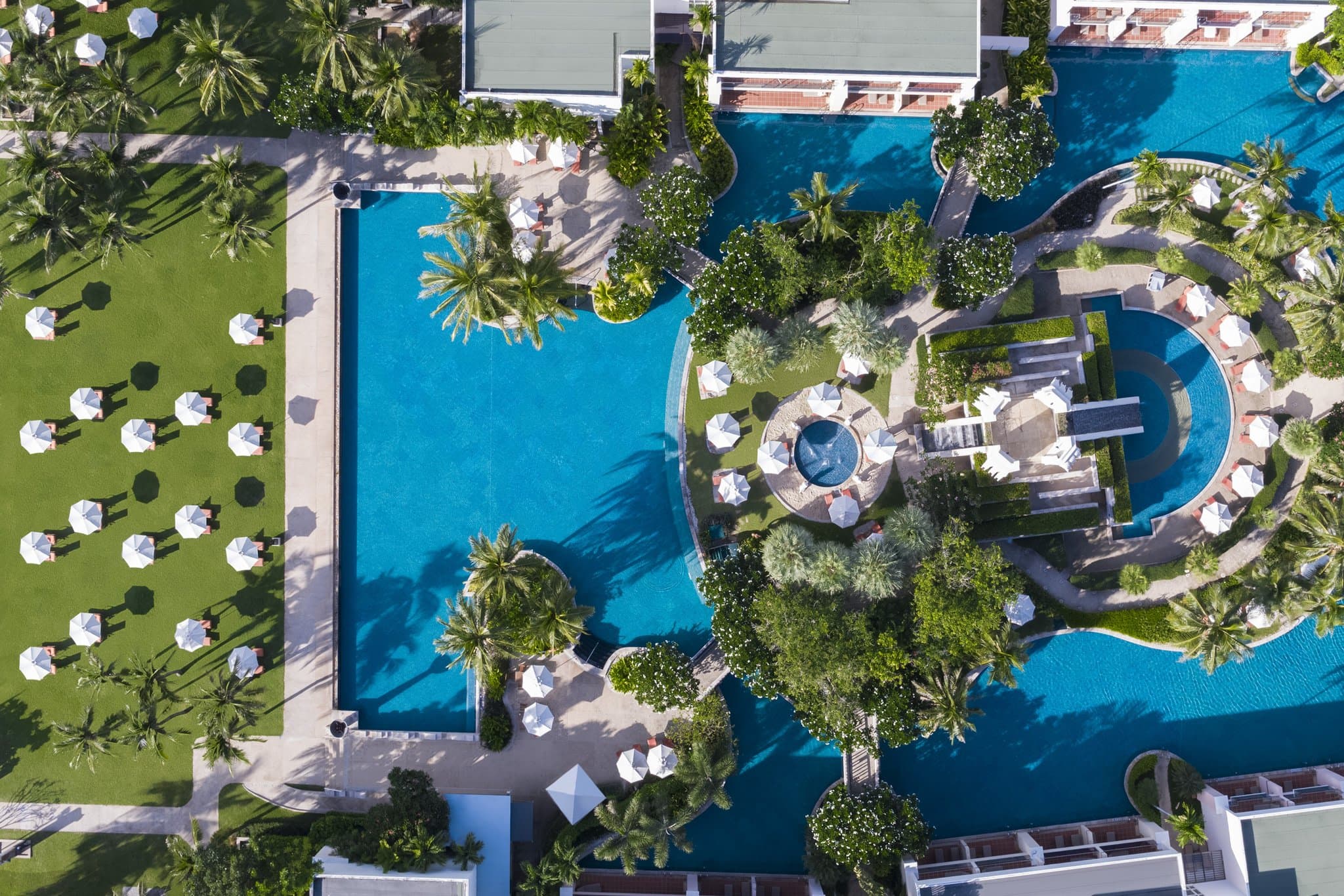 A guest's feet dangling from a private terrace into the winding lagoon pool at Sheraton Hua Hin, surrounded by tropical foliage.