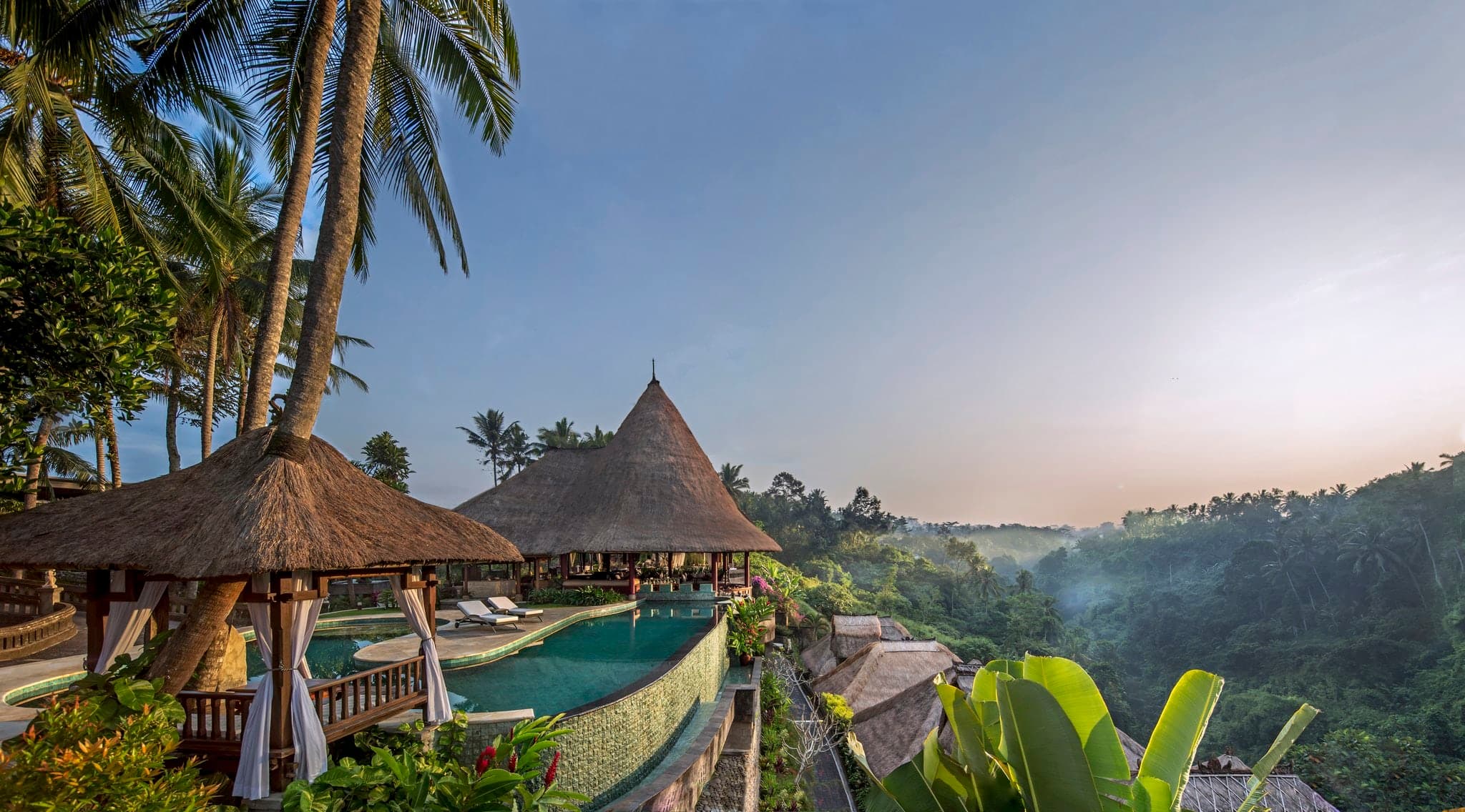 A heated infinity pool at Viceroy Bali hovering over the Petanu River gorge, with a thatched-roof villa and dense jungle in the background.