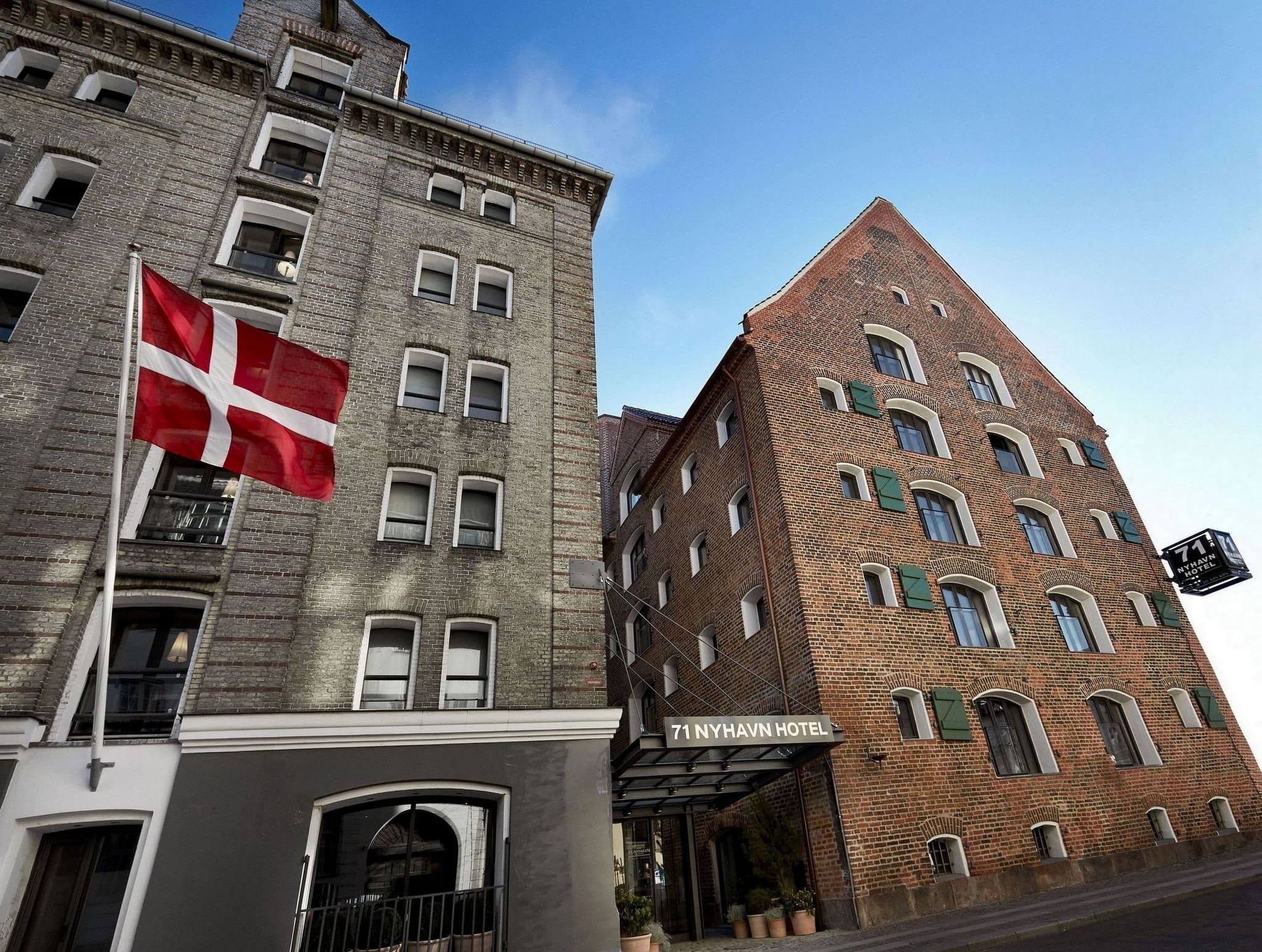 Interior of 71 Nyhavn Hotel suite showing exposed rustic timber beams, white walls, and a window view of the Copenhagen harbor.