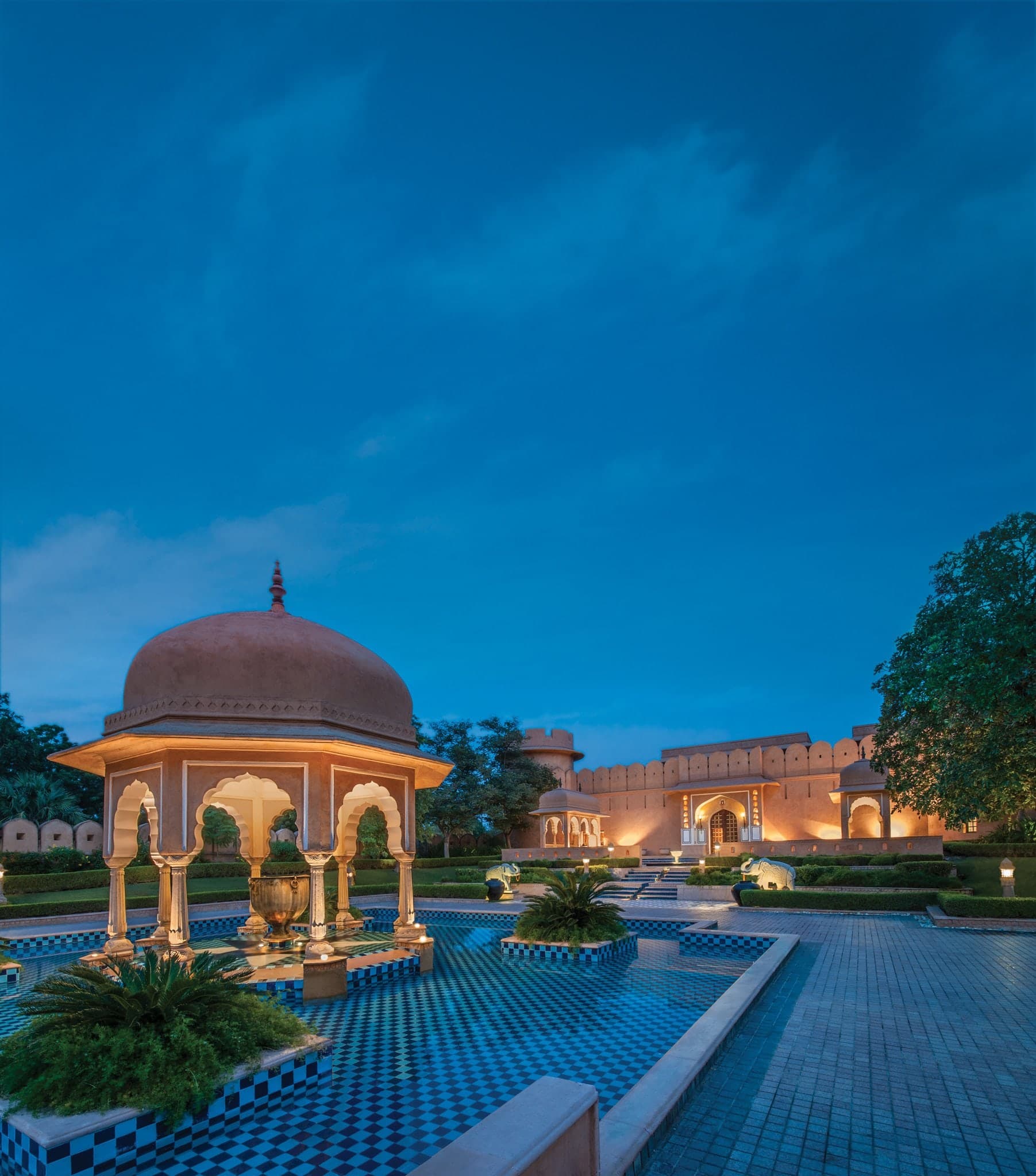 Golden hour light hitting the 280-year-old Shiva temple at The Oberoi Rajvilas, framed by manicured hedges and a wandering peacock.