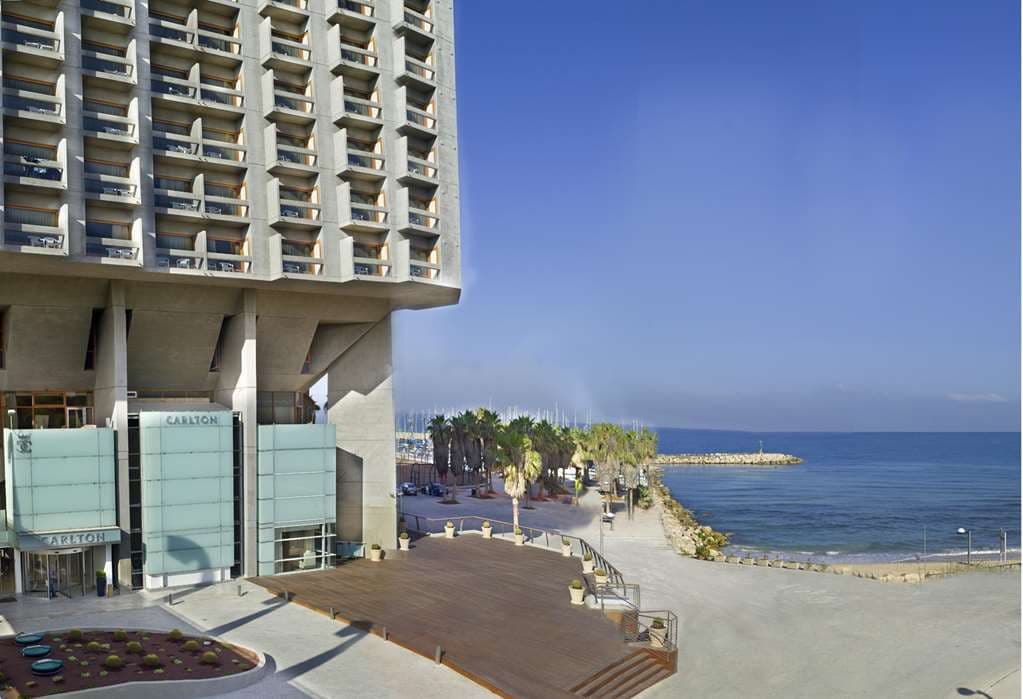 The Carlton Tel Aviv rooftop pool deck at sunset, overlooking the Mediterranean marina and city skyline.