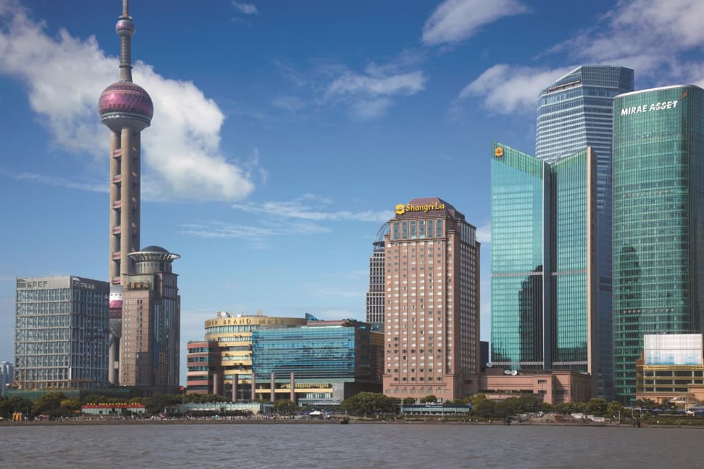 A sleek, modern hotel room in the Grand Tower with floor-to-ceiling windows framing the Oriental Pearl Tower and the Bund across the river.