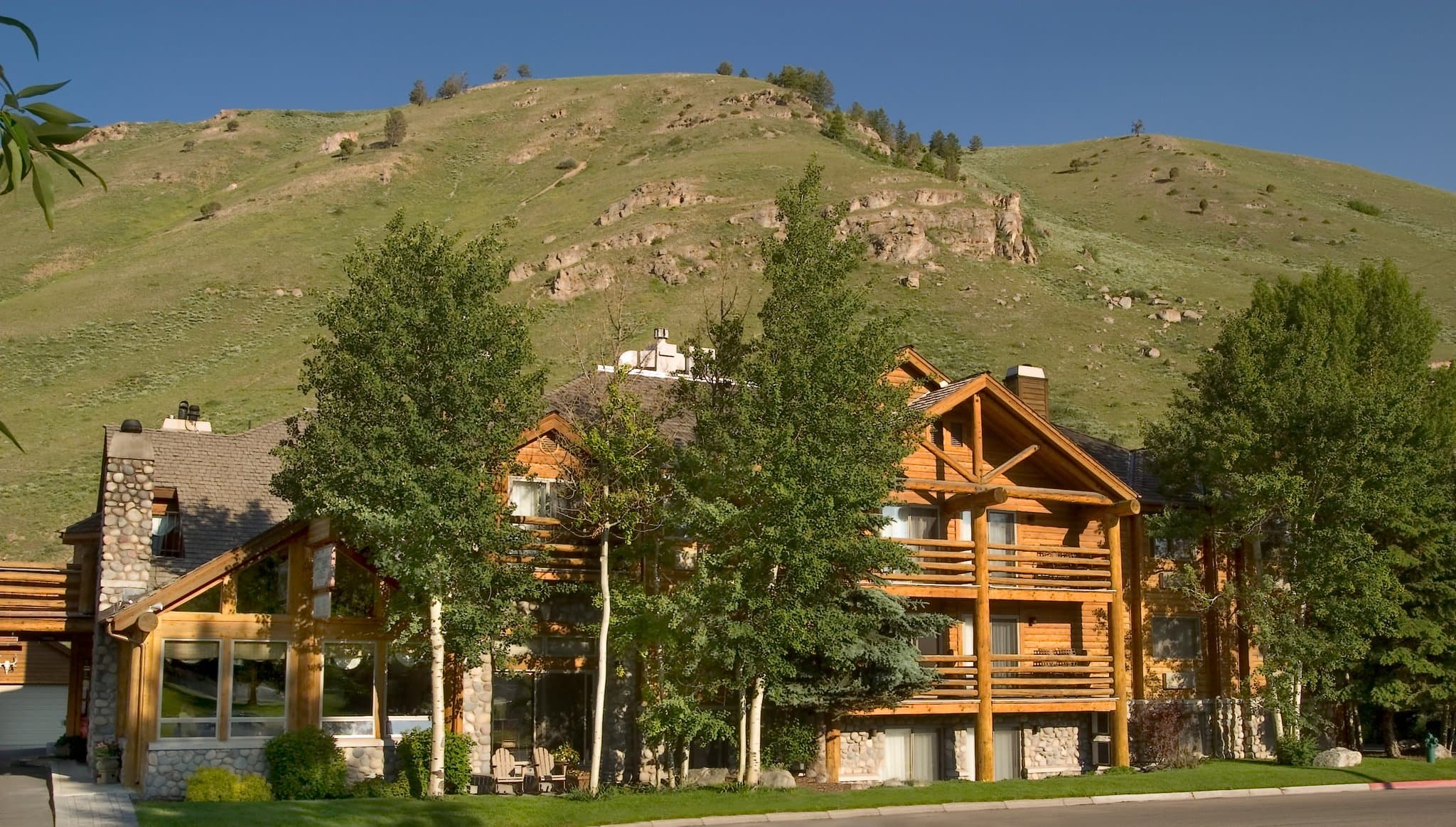 A cozy, upscale lodge bedroom with a stone fireplace, leather armchairs, and a view of the Wyoming mountains.