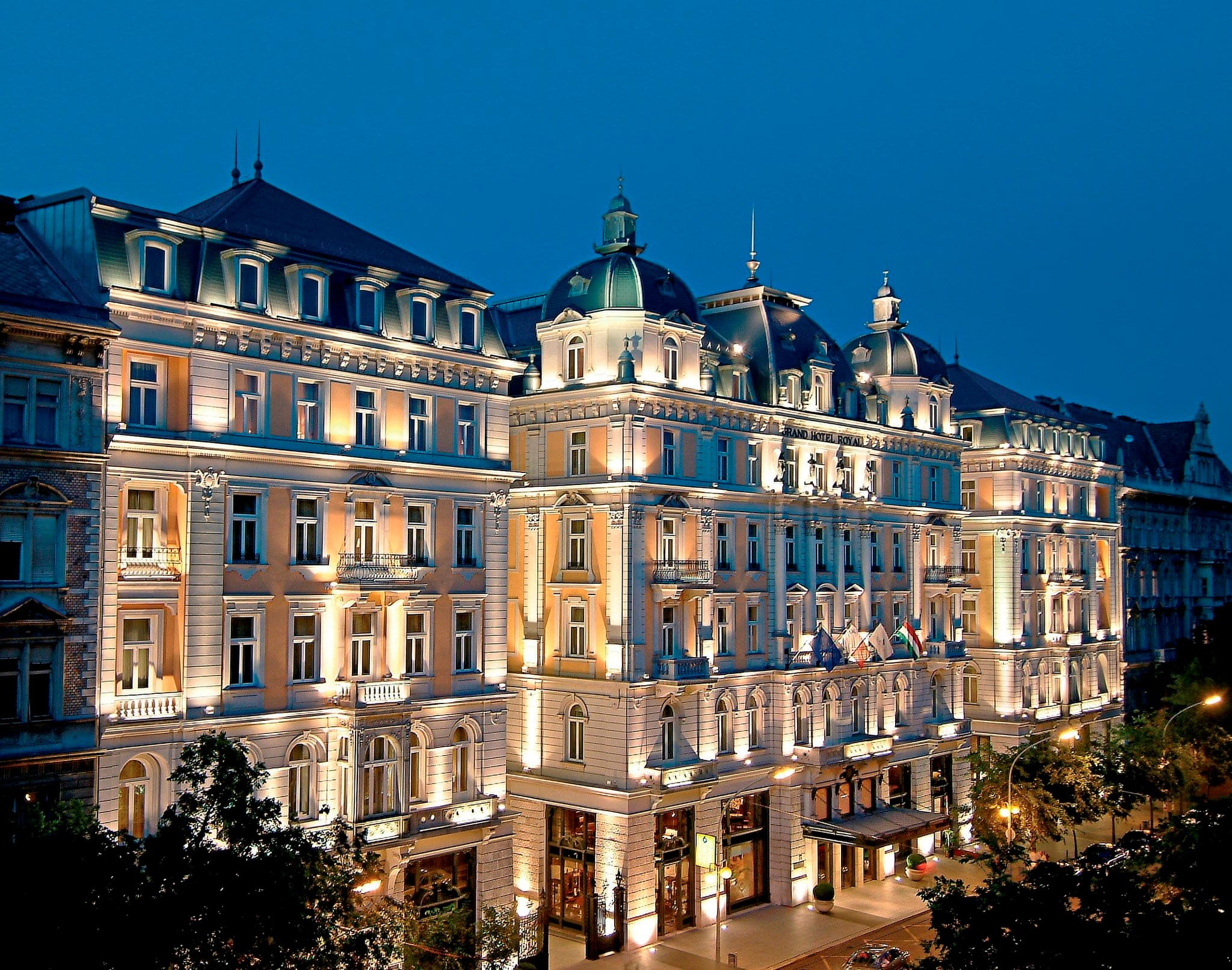 The iconic Royal Spa indoor pool at Corinthia Budapest featuring turquoise water, Corinthian columns, and a vaulted stained-glass ceiling.