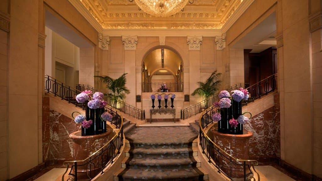 The Peninsula New York's grand lobby staircase featuring the new Bill Rooney Studio interior renovation and crystal chandelier.