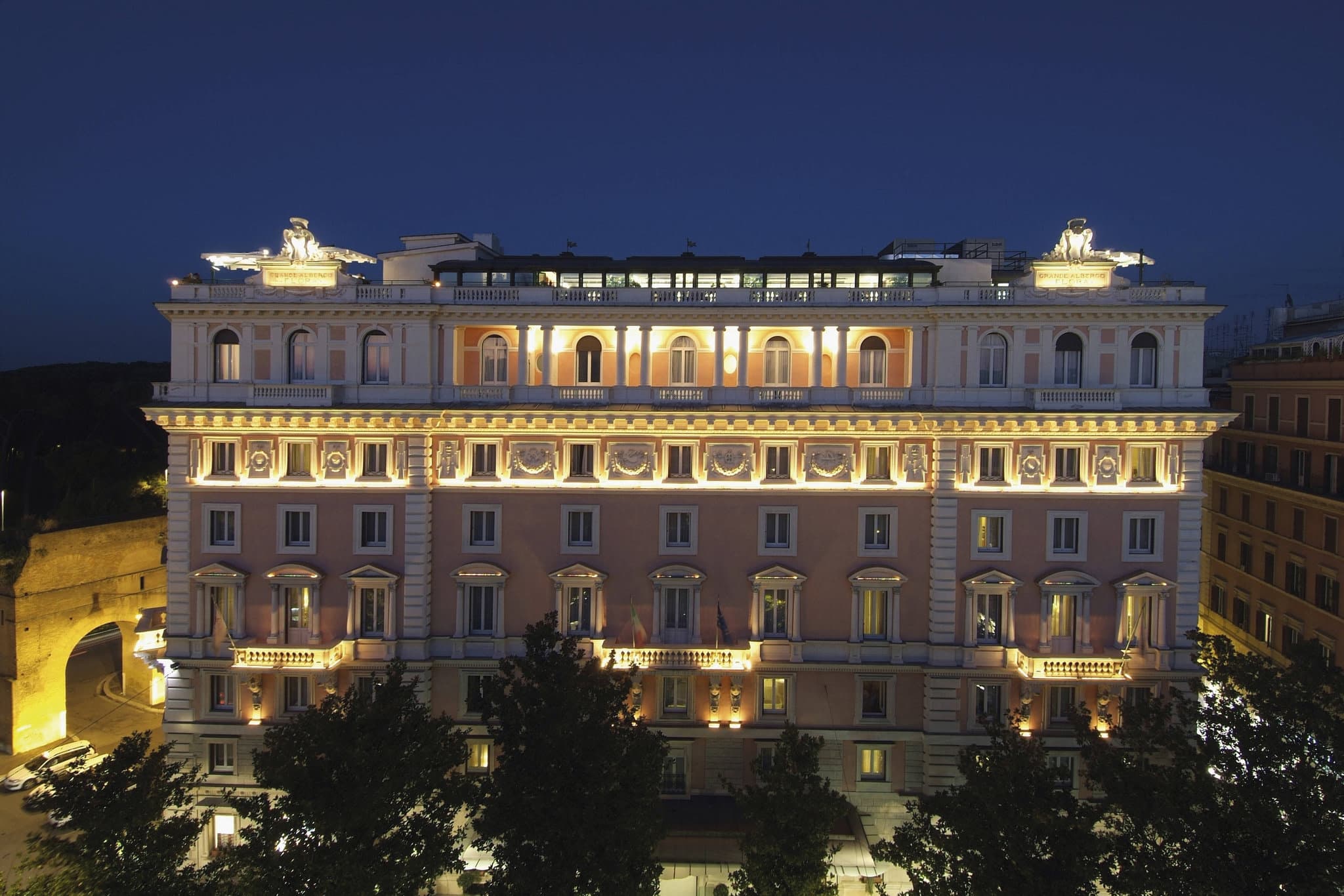 A sweeping view of the Rome Marriott Grand Hotel Flora's rooftop terrace at sunset, set with white tablecloths and overlooking the dome of St. Peter's Basilica and the greenery of Villa Borghese.