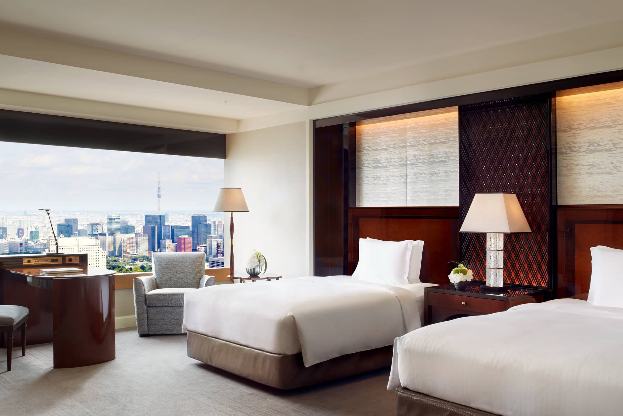 The moody, high-ceilinged lobby of The Ritz-Carlton Tokyo on the 45th floor, featuring heavy timber columns, plush seating, and floor-to-ceiling windows overlooking the Tokyo Tower and skyline at night.