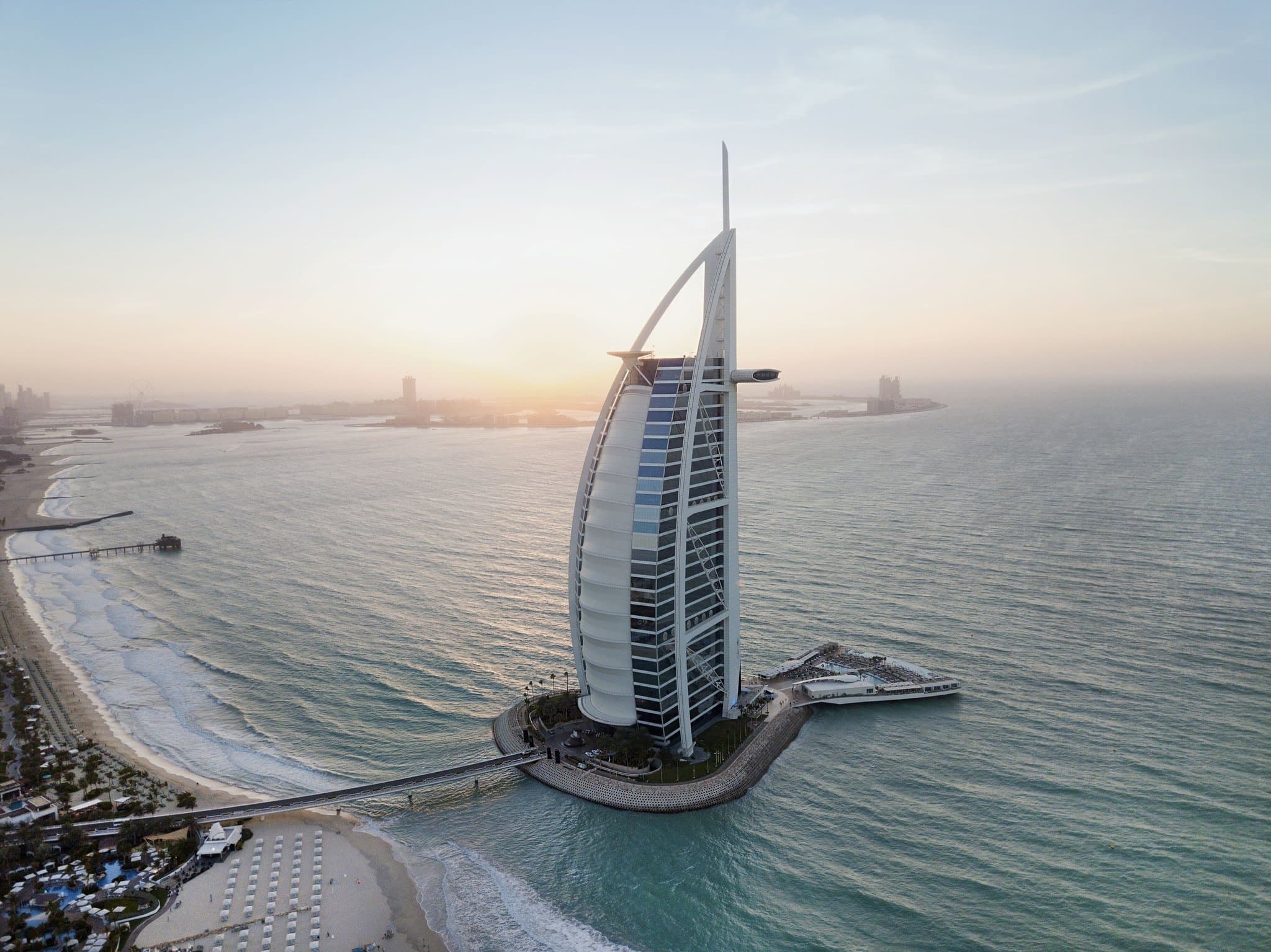 The Burj Al Arab Jumeirah sail-shaped exterior rising from a private island against a clear blue Dubai sky.