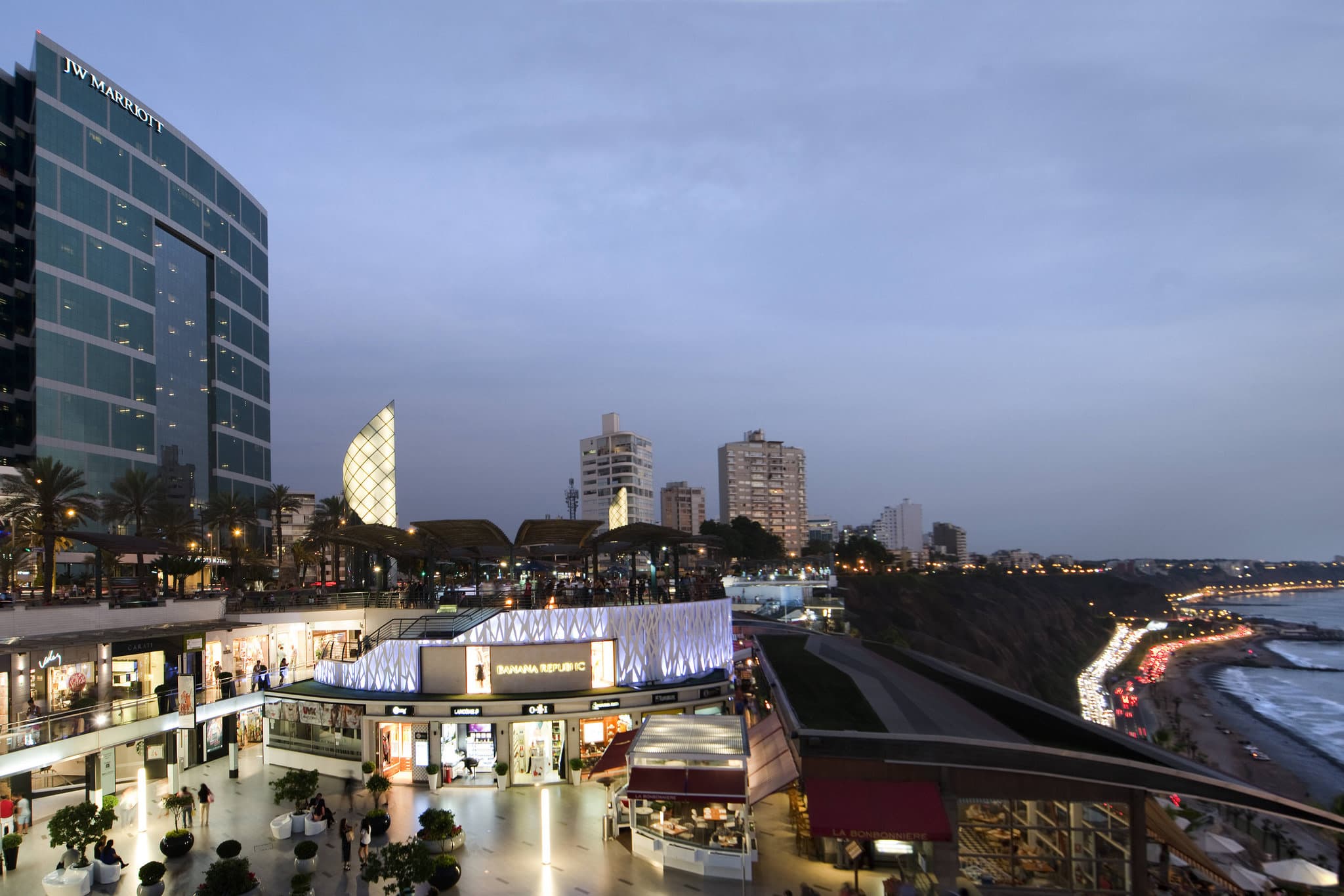 The curved glass exterior of the JW Marriott Hotel Lima reflecting the sunset, perched above the Costa Verde cliffs.