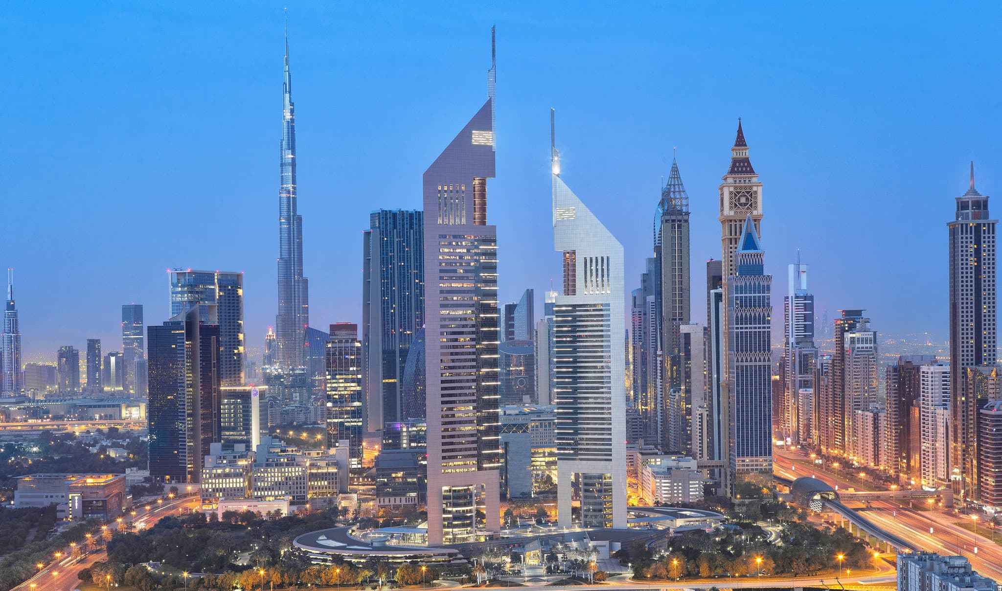 The illuminated twin triangular towers of Jumeirah Emirates Towers piercing the night sky above Dubai's financial district.
