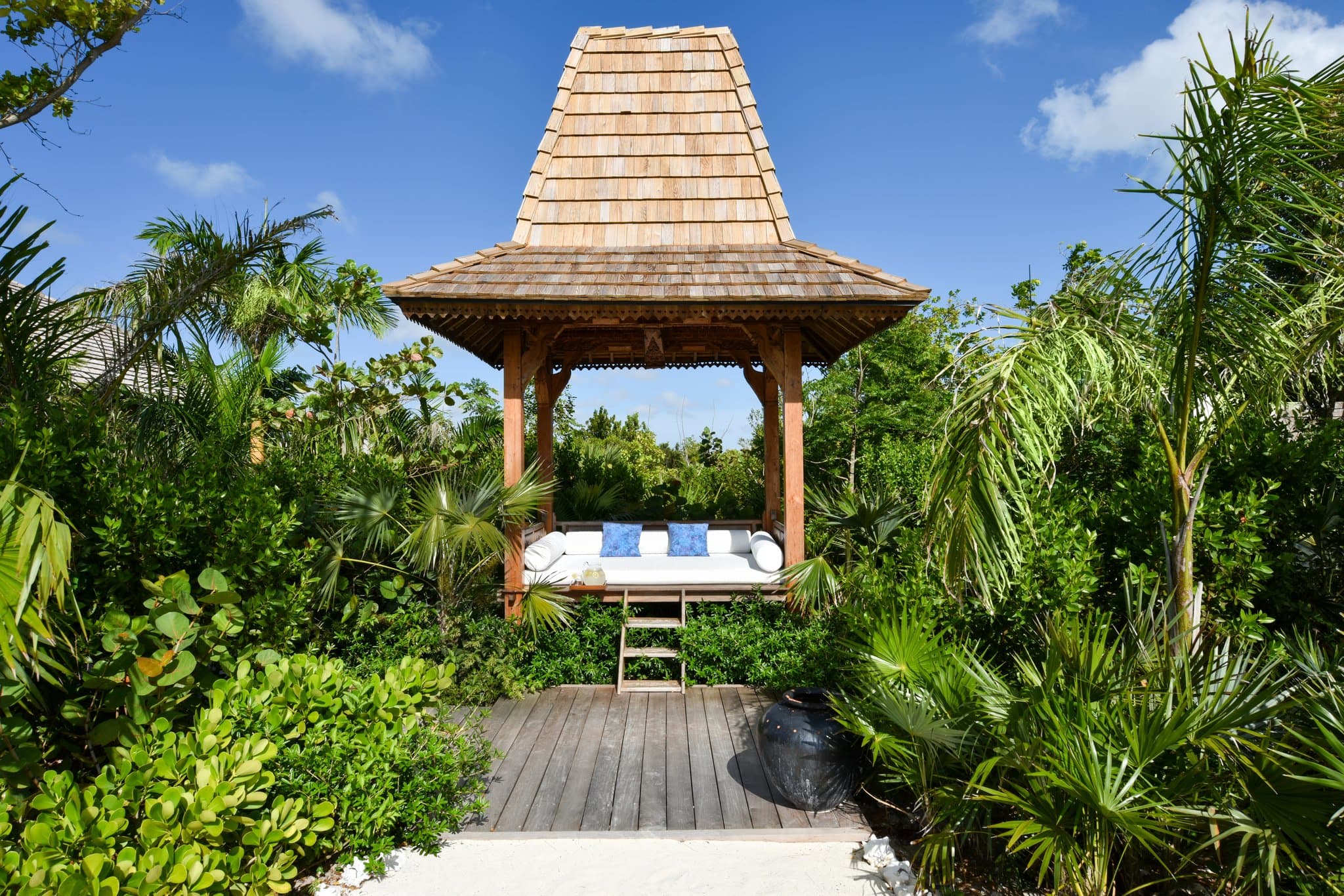 A minimalist wooden boardwalk leading towards a turquoise ocean at COMO Parrot Cay, flanked by lush green mangroves under a clear blue sky.