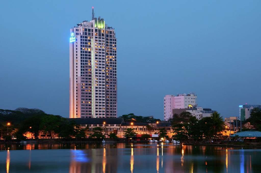 Twilight view of the Level 3 outdoor pool at Hilton Colombo Residences with illuminated turquoise water and city skyline.