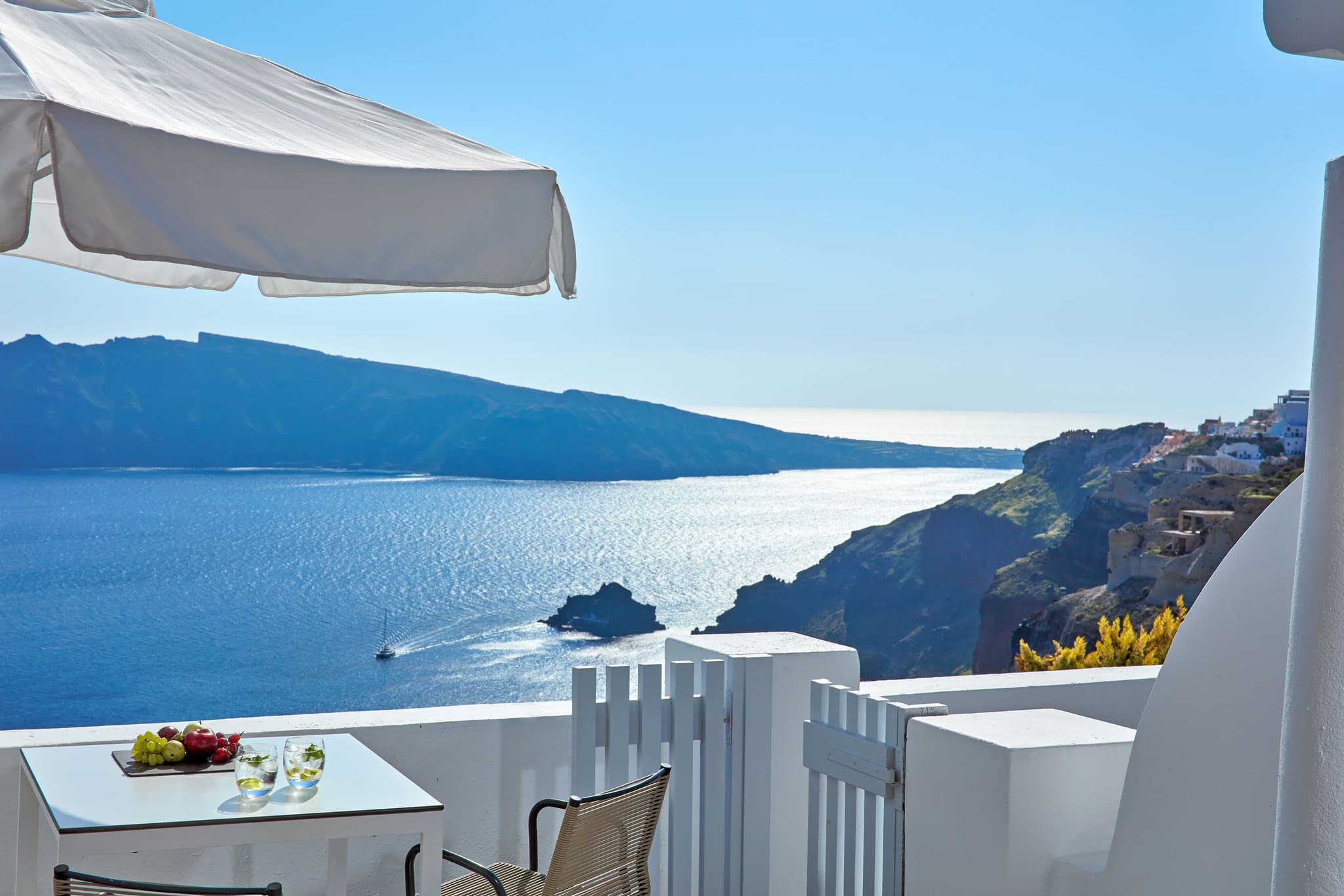 Katikies Santorini's signature white pedestrian bridge arching over a turquoise infinity pool with the caldera in the background.