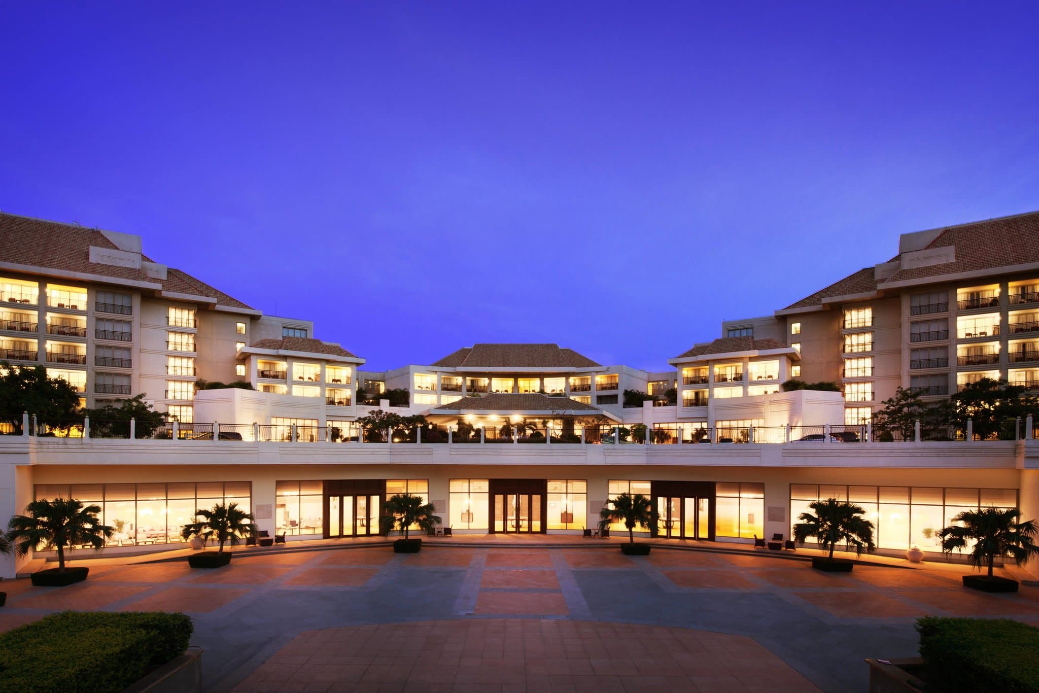 A lush, palm-lined lagoon pool at Sanya Marriott Yalong Bay leading directly to a white sandy beach with blue umbrellas.
