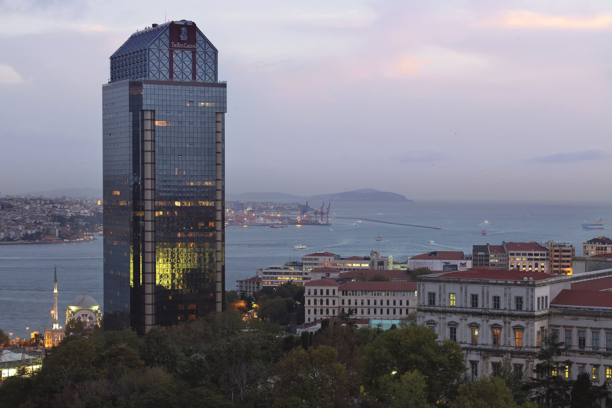A guest relaxing in a wooden window nook at The Ritz-Carlton Istanbul, overlooking the Bosphorus Strait and Vodafone Park.