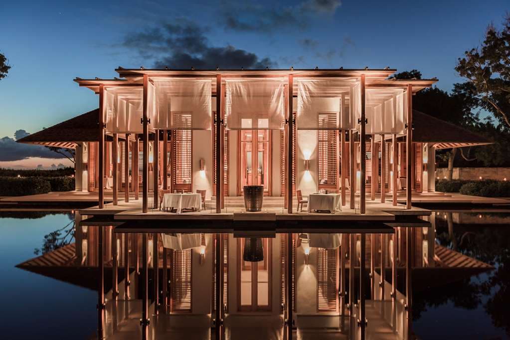 Amanyara's iconic circular bar pavilion reflected in a tranquil pond at dusk, surrounded by mahogany trees.