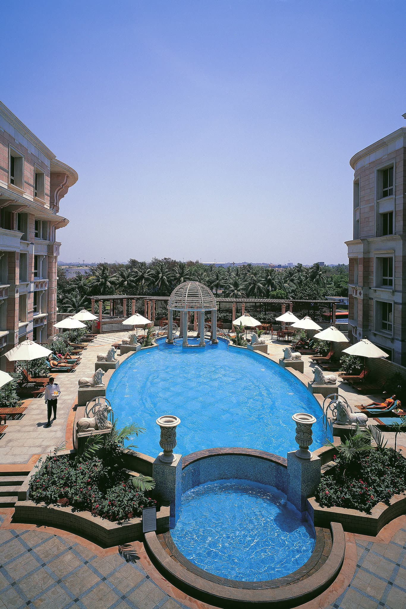 Sun-drenched atrium of ITC Maratha Mumbai featuring a grand staircase, central dome, and wooden horse sculptures.